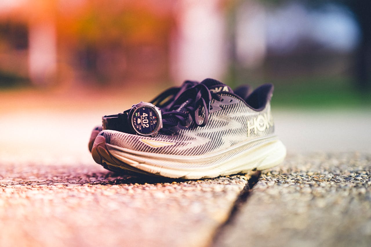 hero-img-02 A pair of Hoka running shoes with a Garmin watch beside them on a sunny outdoor track.